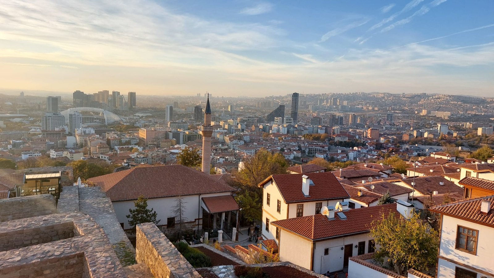 Golden hour view from a hilltop over old tiled houses, a minaret and the modern high-rise skyline of Ankara