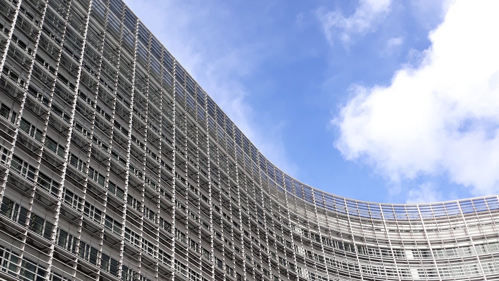 Curved glass and steel facade of the Berlaymont rising against blue sky and white clouds