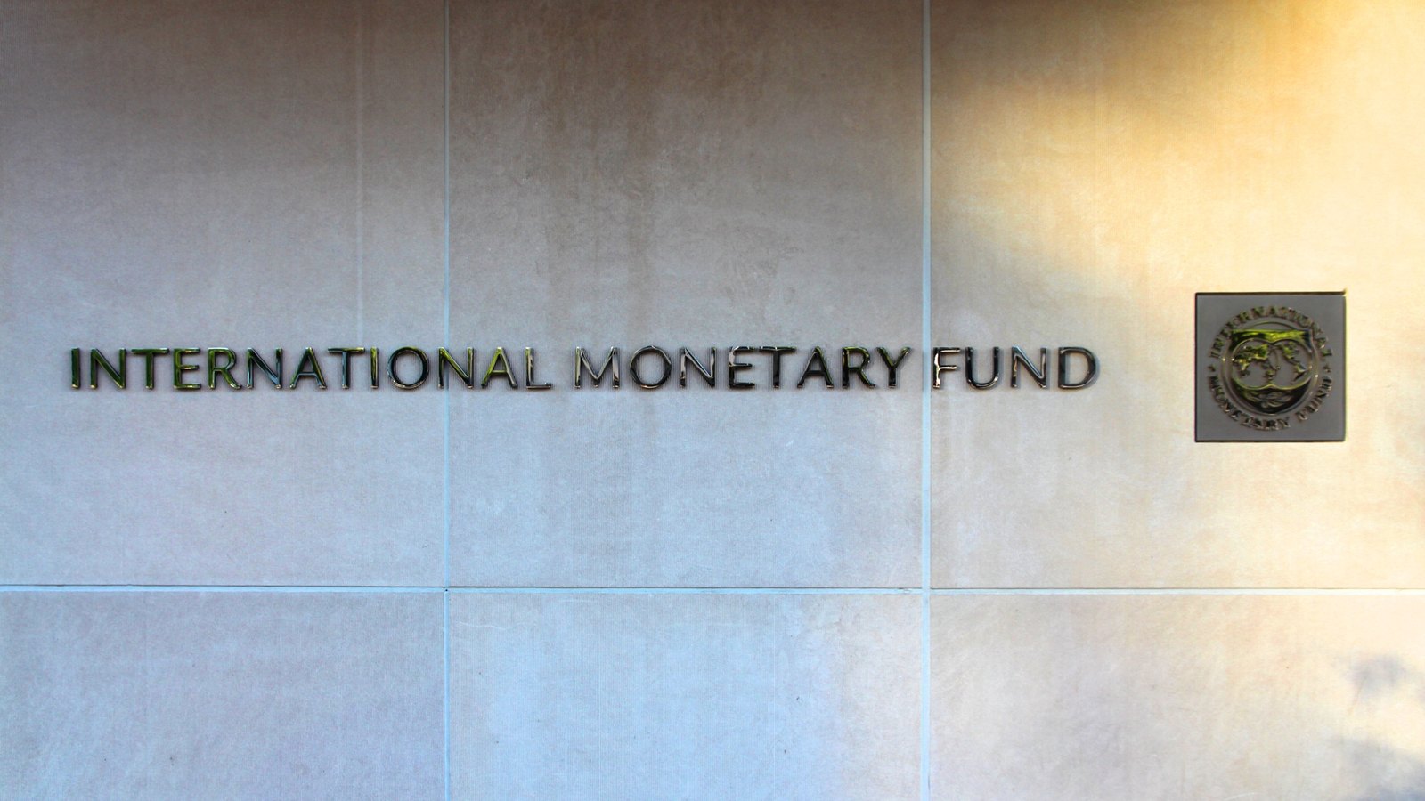 Metal lettering reading International Monetary Fund with the fund's seal on a stone wall