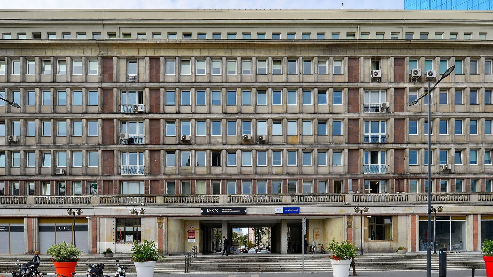 A long stone office block with rows of windows, a central entrance and bicycles parked out front