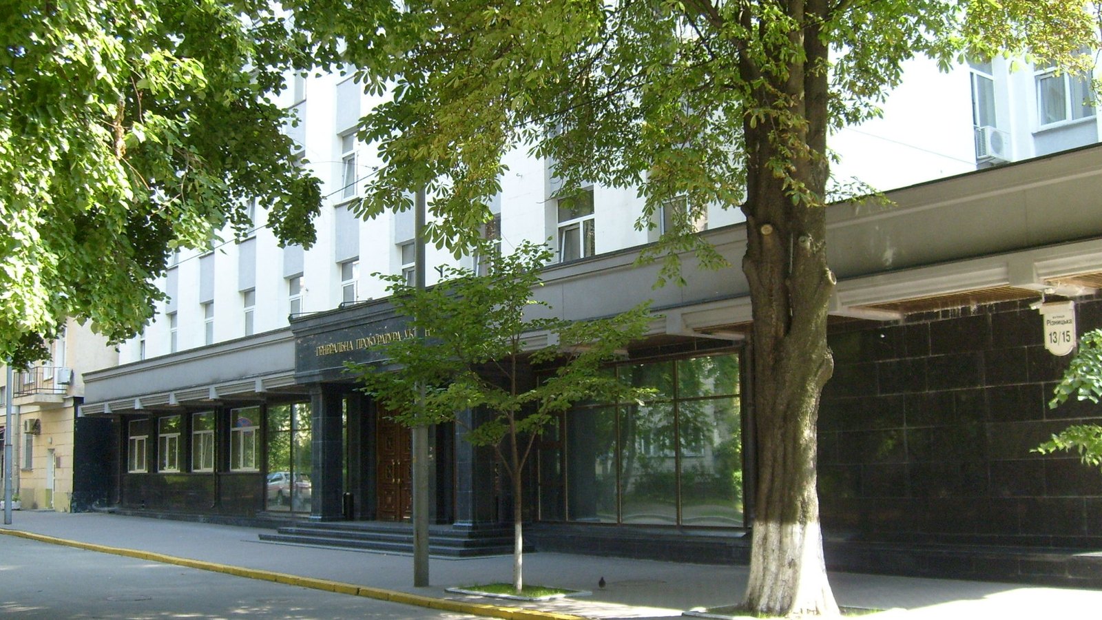 A large grey office building on a street, with trees in front