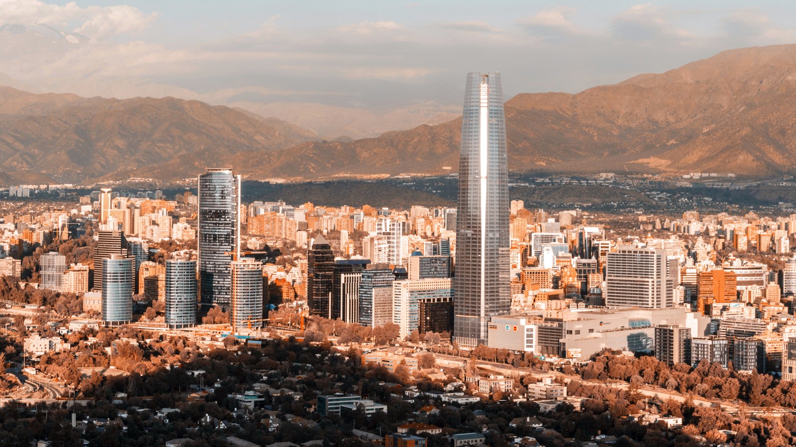 A dense city of towers spreading towards mountains under a hazy sky