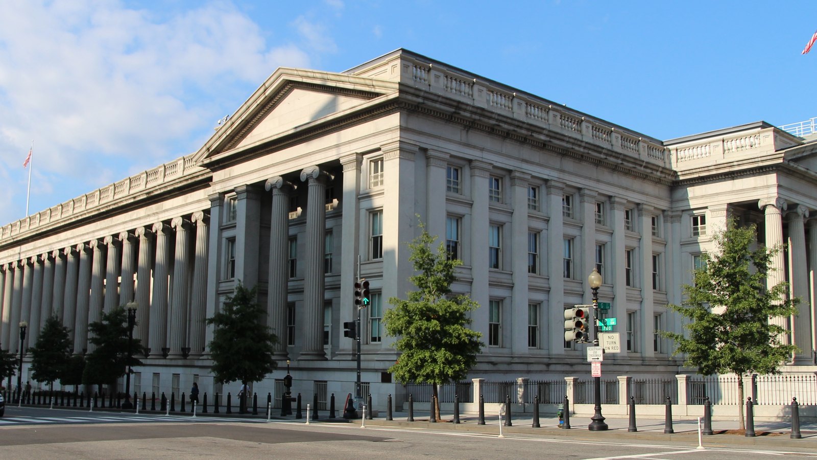 Long granite colonnade of the Treasury Building on a sunny day, with trees and street lamps along the pavement
