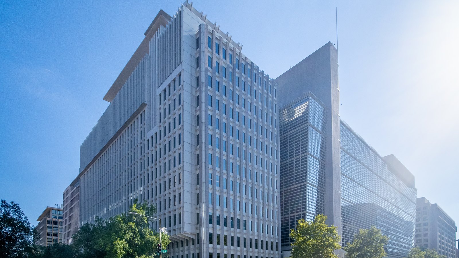 World Bank headquarters, a white high-rise beside a glass tower on a street corner under a bright blue sky